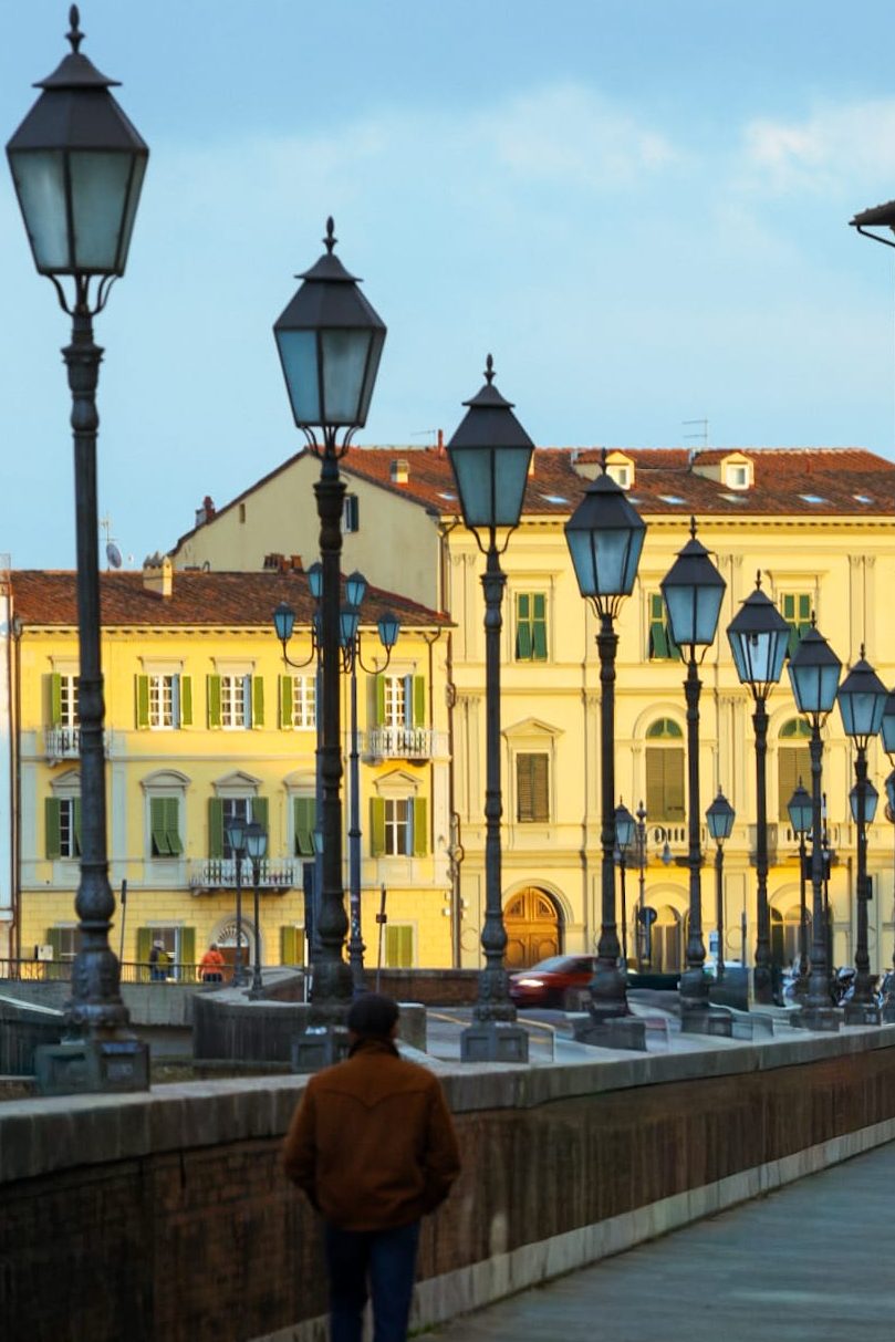 Persona che cammina lungo un ponte a Pisa tra una fila di lampioni.
